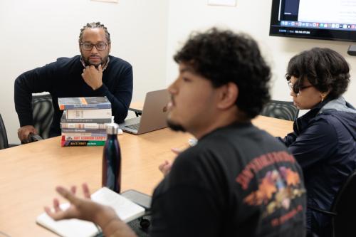 Professor Quito Swan listening to a student speak in a classroom seated at a shared table
