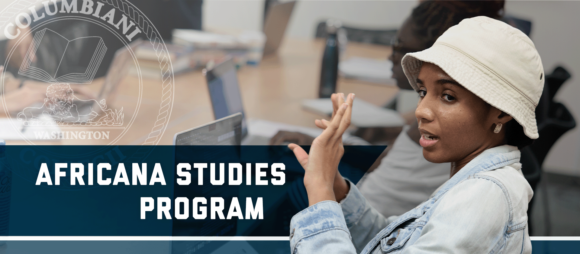 Close-up of a student talking at a classroom table, wearing a bucket hat