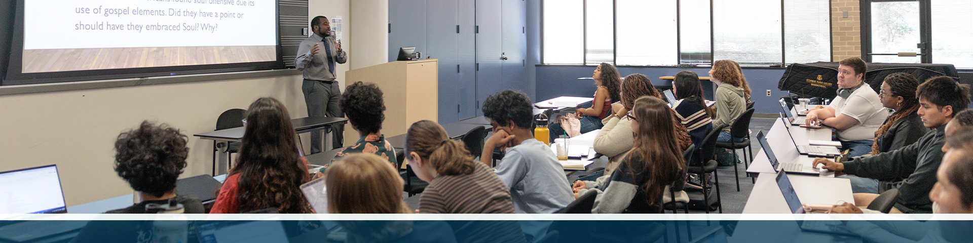 A professor standing in front of a lecture hall presenting slides to students